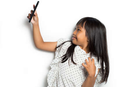 Cute asian little girl taking selfie with a smartphone camera on white backgroundの写真素材