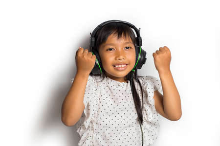 Asian Little girl with headphones listening music enjoy and dance on white backgroundの写真素材