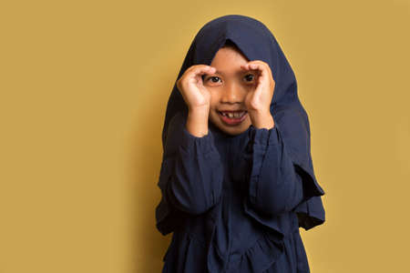 Asian little muslim girl wearing hijab peeking through fingersの写真素材