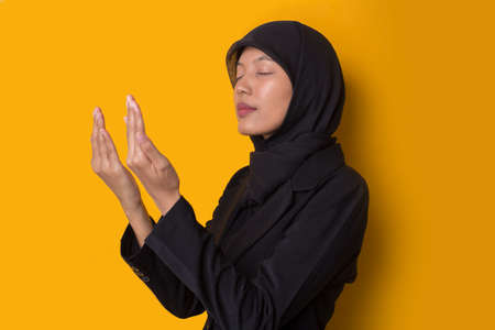 Young asian muslim woman with hijab praying on yellow backgroundの写真素材