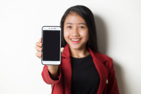 Happy Asian business woman demonstrating mobile cell phone. Portrait of smiling girl, posing on white backgroundの写真素材