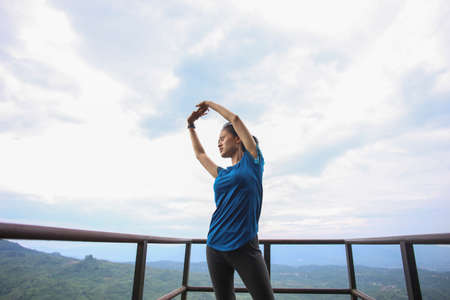 Portrait of fit and sporty young asian woman doing stretching on the mountain.の写真素材
