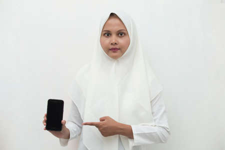 Happy Asian woman in hijab demonstrating mobile cell phone. Portrait of smiling girl