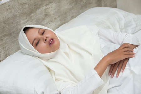 Young asian muslim woman sleeping tired dreaming. Women pretending to sleep and making gesture. Sleepy tired woman falling asleep being exhausted.の写真素材