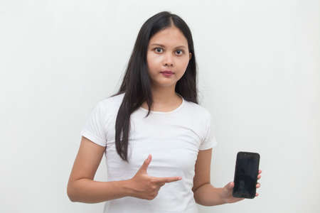Happy Asian woman demonstrating mobile cell phone. Portrait of smiling girl, posing on white backgroundの写真素材