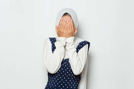 Asian muslim woman covers her face with her hands