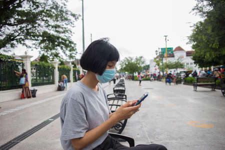 Young asian woman with face mask using mobile phone in public spaces.の写真素材