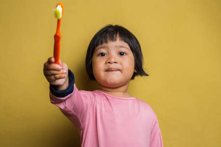 asian little girl brush her teeth isolated on yellow backgroundの写真素材