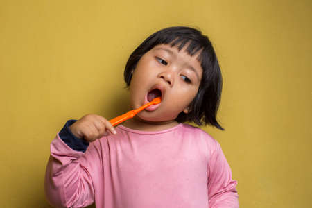asian little girl brush her teeth isolated on yellow backgroundの写真素材