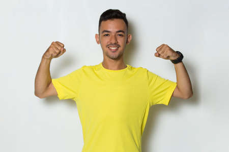young  sporty man dressed in yellow tshirt showing strong gesture on white backgroundの写真素材