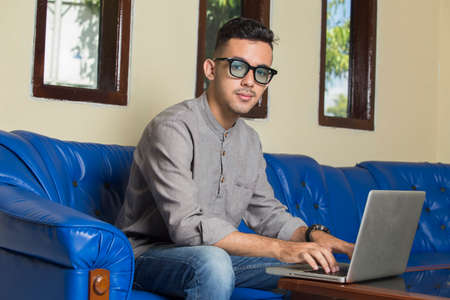 young handsome man sitting on sofa at home working on laptop online