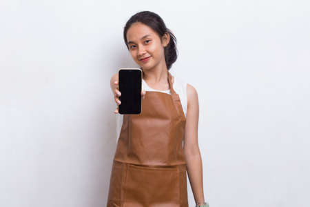 Beautiful Asian Barista waitress demonstrating mobile cell phone on white backgroundの写真素材