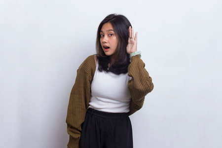 Young beautiful asian woman with hand over ear listening an hearing to gossip isolated on white backgroundの写真素材