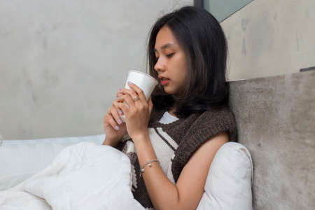 sick young asian beautiful woman drinking water in bedの写真素材