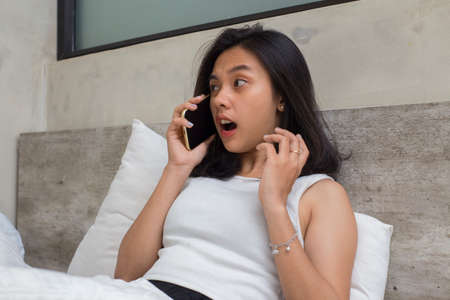 unhappy asian beautiful girl feeling sad using  smartphone on bedの写真素材