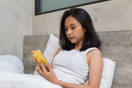 unhappy asian beautiful girl feeling sad using  smartphone on bedの写真素材
