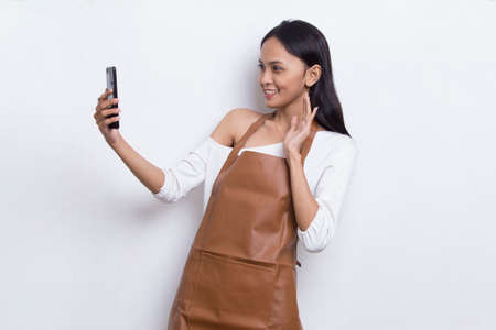 Young asian woman bartender or waitress using mobile smartphone isolated on white backgroundの写真素材