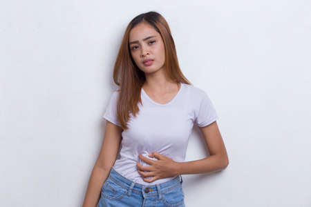Sick asian beautiful young woman having a stomach ache isolated on white backgroundの写真素材