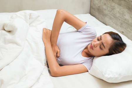 Young asian woman sleeping and having a stomach acheの写真素材