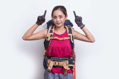 Young asian hiker woman with backpack pointing finger on empty space on white backgroundの写真素材