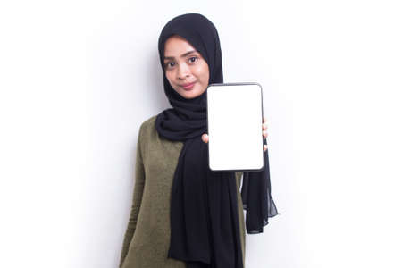 young beautiful asian muslim woman demonstrating mobile cell phone isolated on white backgroundの写真素材