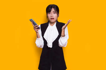 mad and shock young asian beautiful woman using mobile phone isolated on yellow backgroundの写真素材