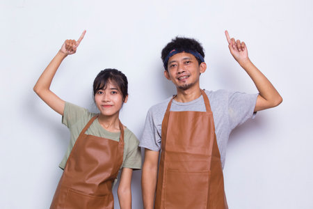 Asian couple barista waiter wears apron pointing with fingers to different directions isolated on white backgroundの写真素材