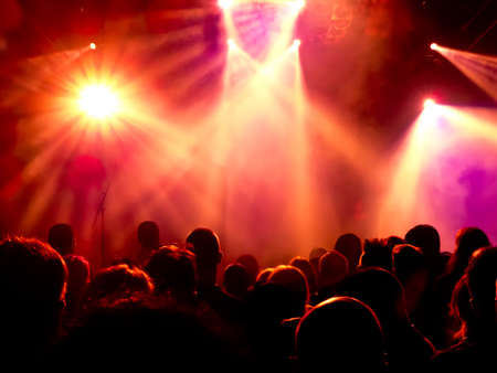 silhouettes of concert crowd in front of bright stage lightsの写真素材