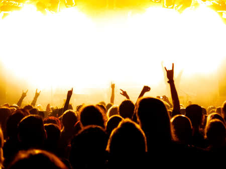 silhouettes of concert crowd in front of bright stage lightsの写真素材