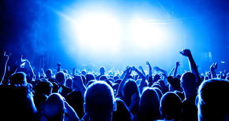 silhouettes of concert crowd in front of bright stage lightsの写真素材