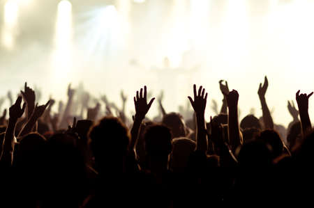 silhouettes of concert crowd in front of bright stage lightsの写真素材