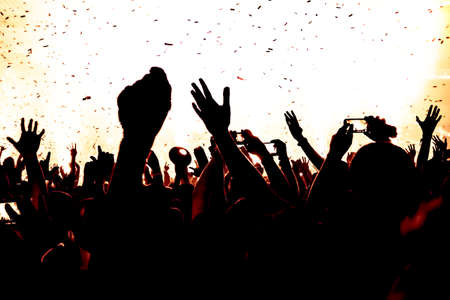 silhouettes of concert crowd in front of bright stage lightsの写真素材