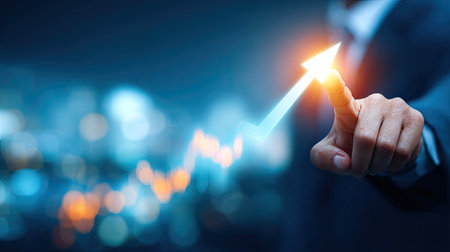 Shot features a person's hand, likely a business professional in a suit, interacting with a bright, glowing digital arrow pointing sharply upwards, indicating positive progress or rising statistics against a blurred, dark blue background filled with abstract, out-of-focus city lights.の素材
