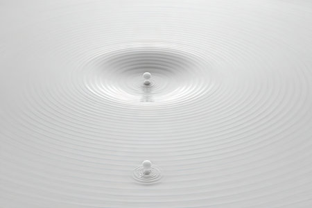 Close-up view of two small white spheres impacting a smooth, rippled surface.  The impact creates concentric ripples radiating outward from the points of impact. The overall effect is clean, elegant, and visually interesting.の素材