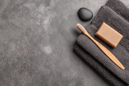 Gray stone surface is the backdrop for a dark gray towel, a natural soap bar, and a wooden toothbrush.  The items are arranged in a simple, visually appealing way.の素材