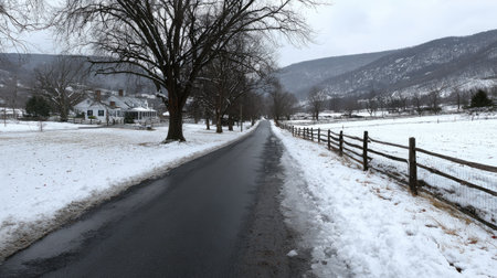 A winter road leads to a farmhouse with mountains in the background.の素材