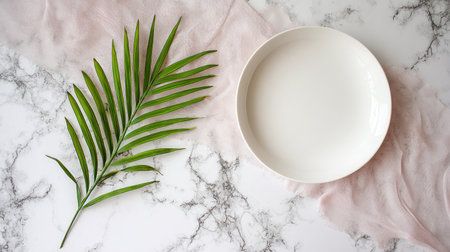 Overhead flat lay presents a pristine white, shallow round plate positioned to the right, next to a vibrant green, segmented palm leaf on the left. The foundation is a white and gray veined marble surface, partially covered by a swath of sheer, pale pink draped cloth, creating an elegant, minimalist composition ideal for food presentation or aesthetic backgrounds.の素材