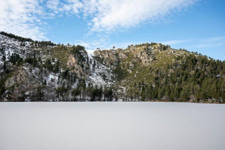 the serene beauty of a winter landscape at Querigut Pond in the Pyrenees, Ariege, France. The pond's surface is frozen, covered in a blanket of snow, creating a picturesque sceneの写真素材