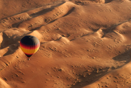 Colorful hot air balloon soaring above the golden dunes of the Middle Eastern desert, showcasing a popular tourist activity.の写真素材