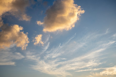 Fluffy orange and white clouds against a vivid blue sky create a captivating background, ideal for presentations, website banners, or adding depth to your creative projects.の写真素材