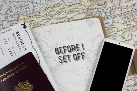A travel journal is open to the 'BEFORE I SET OFF' page, showing a passport, boarding pass, and smartphone against a vintage map, setting the scene for an exciting journey. Key travel documents and tech essentials are neatly arranged, ready for adventure.の写真素材