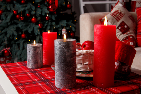 Christmas setting background: four red and silver burning candles, decorated Christmas tree, red apples in the basket, selective focus.の写真素材