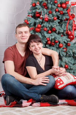 Young and happy family couple sitting near decorated New Year tree. Closeup portrait.の写真素材