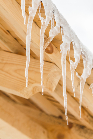 Many beautiful icicles melt on the wooden roof at the end of winter and water drops are fall down. Spring is comming concept.の写真素材