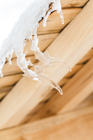 Beautiful icicles in strange form melt on the wooden roof at the end of winter and water drops are fall down. Spring is comming concept.の写真素材