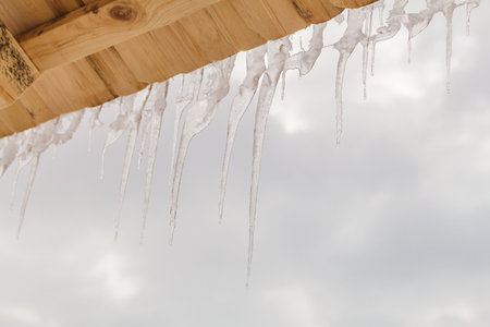 Many beautiful icicles melt on the wooden roof at the end of winter and water drops are fall down. Spring is comming concept.の写真素材