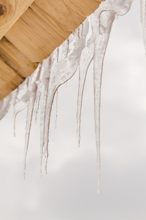Many beautiful icicles melt on the wooden roof at the end of winter and water drops are fall down. Spring is comming concept.の写真素材