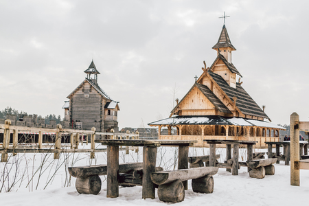 Old wooden table with benches in front of Ancient wooden Slavic church on a snowy landscape. Historical and Architectural Museum in the open air. Kiev, Ukraine. Ancient park Kievskaya Rus'.の写真素材
