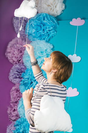 Beautiful and lovely young caucasian girl holding clouds on blue background.の写真素材