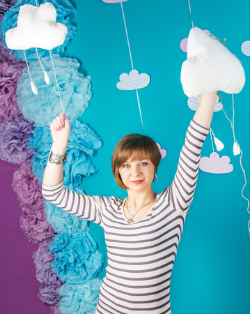 Beautiful and lovely young caucasian girl holding clouds on blue background.の写真素材